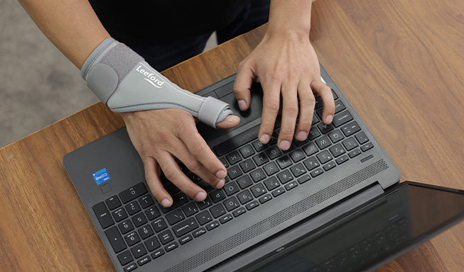 person wear thumb spica splint in his left hand while working on the laptop