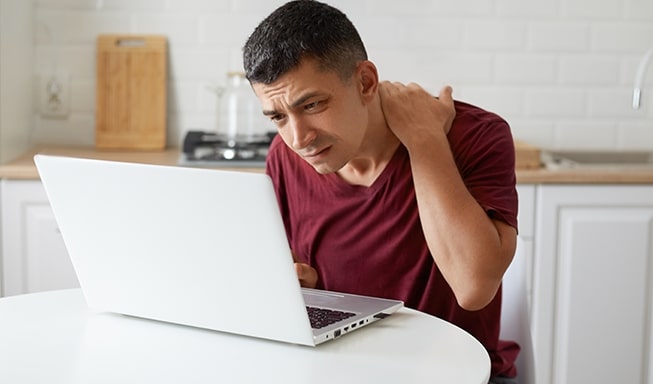 man suffering from neck sprain while working on the laptop