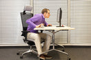 person sitting on a desk working on laptop with bad posture