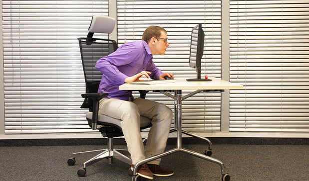 person sitting on a desk working on laptop with bad posture