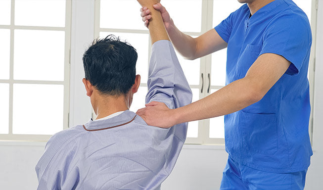 physiotherapist helps the patient in shoulder recovery by exercise