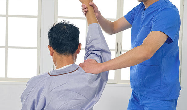 physiotherapist helps the patient in shoulder recovery by exercise