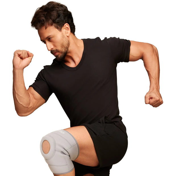 Man flexing muscles wearing a black t-shirt and shorts with a knee wrap